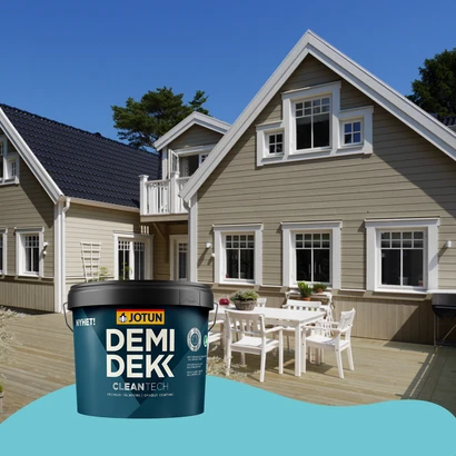 Lichtbruin houten huis met witte kozijnen en donkerblauw dak, geschilderd met Jotun Demidekk CleanTech. Op de voorgrond staat een grote emmer van deze verf op een blauwe ondergrond.