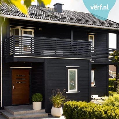 Modern zwart houten huis met witte kozijnen en een houten voordeur, omringd door groene planten in potten. Rechtsboven is het logo van Verf.nl zichtbaar. Het huis is geschilderd met Jotun Demidekk Ultimate Täckfärg.