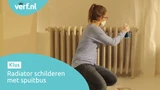 Vrouw met mondkapje en handschoenen verft een radiator met een Hammerite Radiatorlak spuitbus in een afgedekte ruimte. Linksboven het Verf.nl-logo en linksonder de tekst: "Radiator schilderen met spuitbus."