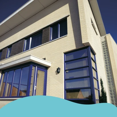 Moderne woning met een gele bakstenen gevel geschilderd met de Sigma Facade Topcoat Satin, donkerblauwe kozijnen en grote raampartijen. De zon schijnt fel op de gevel en er is een helderblauwe lucht op de achtergrond. Onderaan de afbeelding is een grafisc