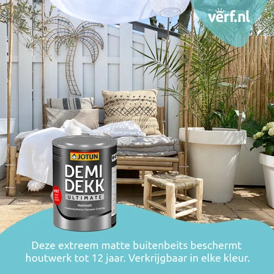 Modern zwart houten huis geschilder met de Jotun Demidekk Ultimate Helmatt op een rotsachtig kustlandschap met uitzicht op zee. Een surfplank staat tegen de gevel en er is een terras met stoelen. Rechtsboven is het Verf.nl-logo zichtbaar.