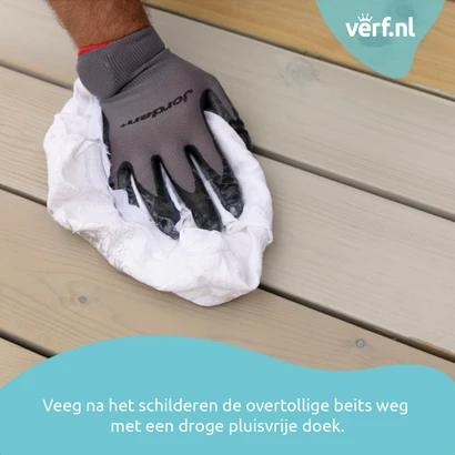 Een hand met een grijze werkhandschoen veegt overtollige Jotun Demidekk Terrasslasyr beits weg van een geschilderd houten terras met een witte pluisvrije doek. Rechtsboven staat het logo van Verf.nl, onderaan de tekst: "Veeg na het schilderen de overtolli