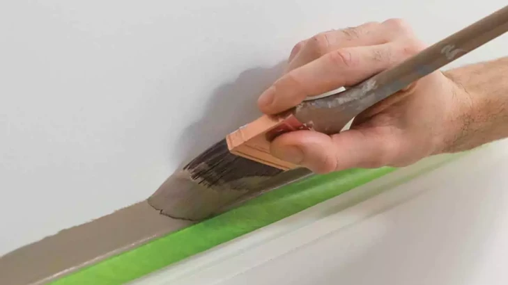 Kwast schildert een strakke lijn langs groene Frogtape op een witte muur.