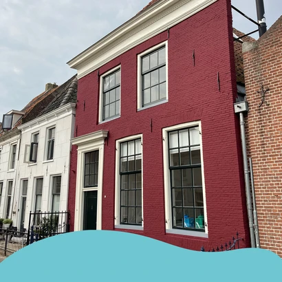 Klassiek herenhuis met rood geschilderde gevel met de Sigma Facade Topcoat Matt en witte kozijnen. De woning staat tussen witte en bakstenen buurpanden in een oude binnenstad. Onderaan een blauwe grafische golfvorm, passend bij de huisstijl van Verf.nl.