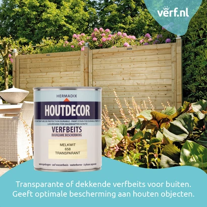 Blik Hermadix Houtdecor Verfbeits in de kleur Melkwit transparant, geplaatst voor een houten tuinscherm en kleurrijke tuinplanten. Ideaal voor duurzame bescherming van hout buitenshuis. Verf.nl-logo rechtsboven.