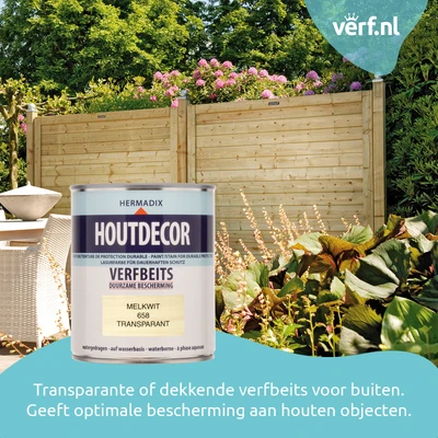 Blik Hermadix Houtdecor Verfbeits in de kleur Melkwit transparant, geplaatst voor een houten tuinscherm en kleurrijke tuinplanten. Ideaal voor duurzame bescherming van hout buitenshuis. Verf.nl-logo rechtsboven.