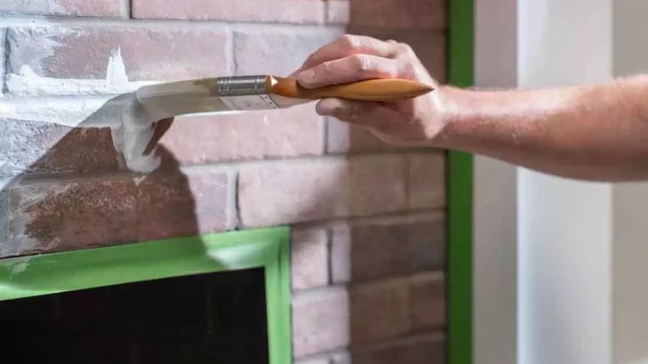 Hand schildert witte verf langs groene Frogtape op bakstenen muur.