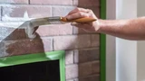 Hand schildert witte verf langs groene Frogtape op bakstenen muur.
