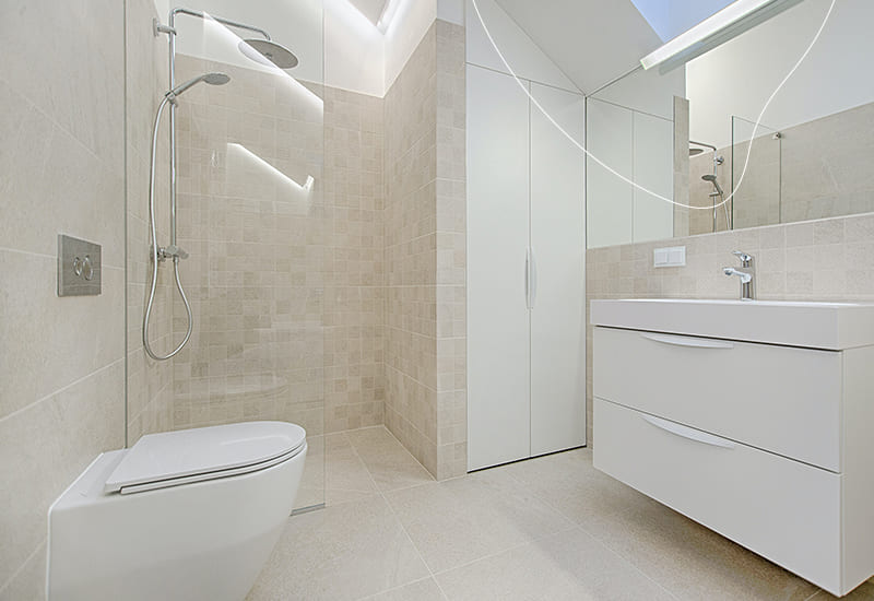 Een betegelde badkamer met een groot wit badkamermeubel, een witte kast, een wit toilet en een douche.
